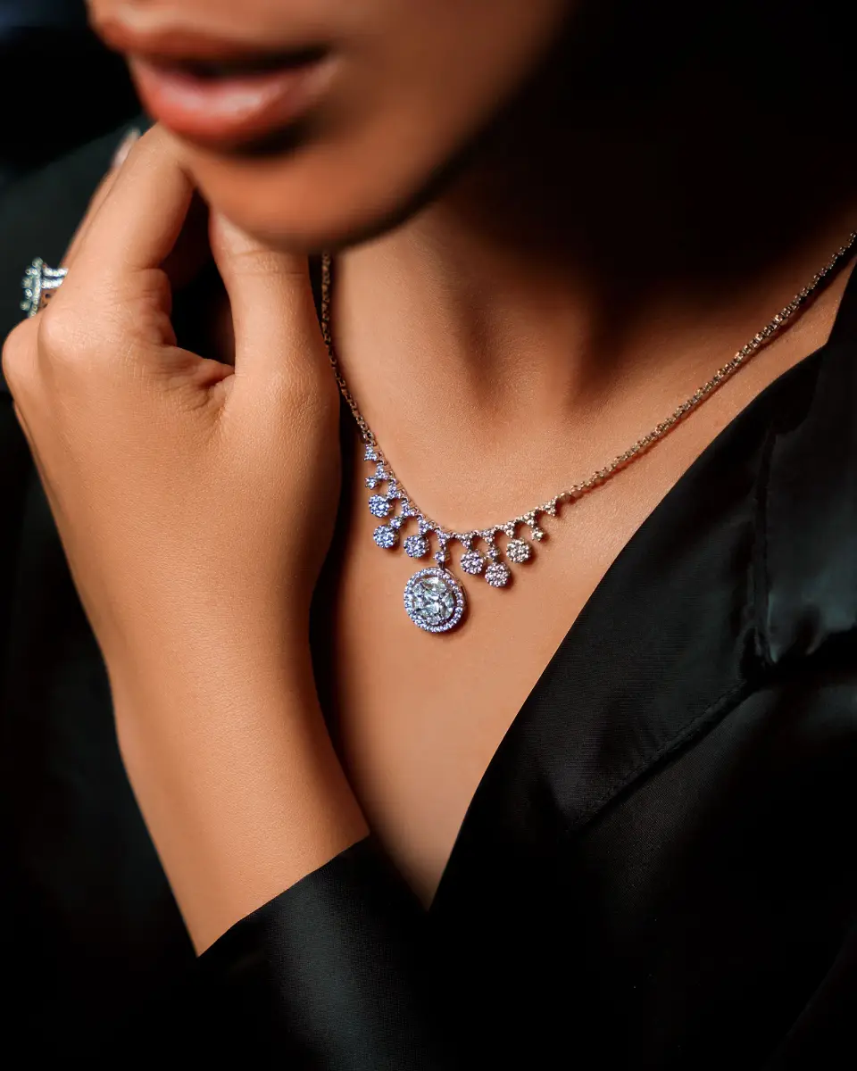 Diamond cluster pendant necklace and a ring on a woman in black satin, close-up