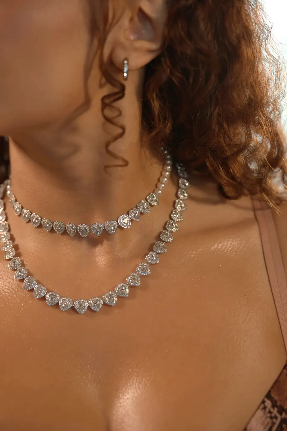 Two diamond riviere necklaces and a drop earring on a woman with curly hair, close-up