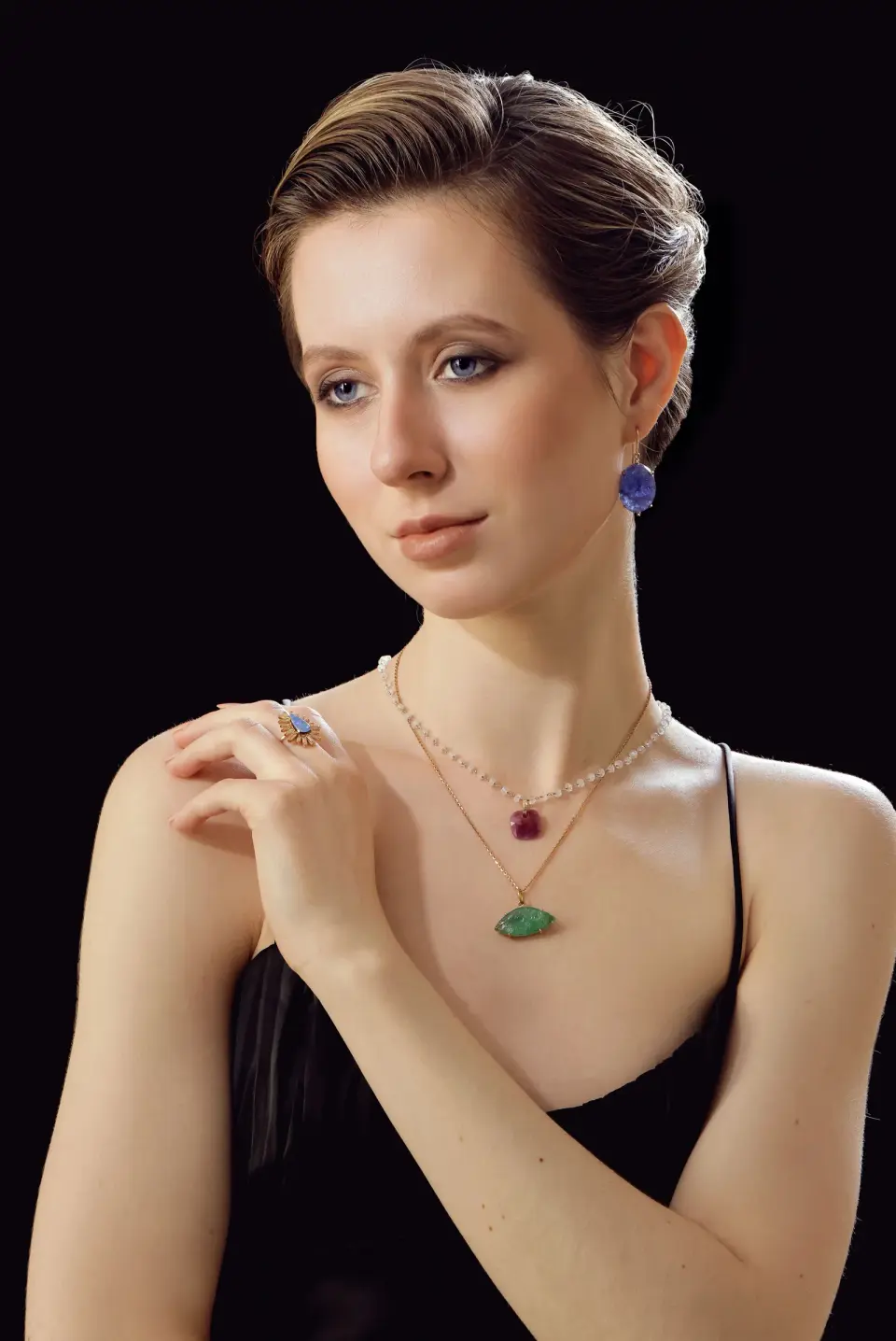 Woman wearing layered gold necklaces with ruby and emerald pendants and a sapphire earring