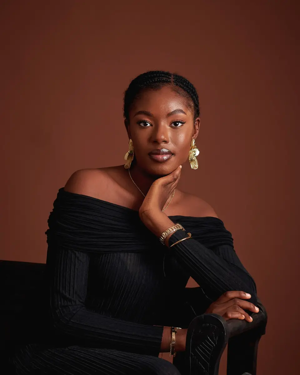 Woman in a black off-shoulder top wearing gold statement earrings and stacked gold bracelets