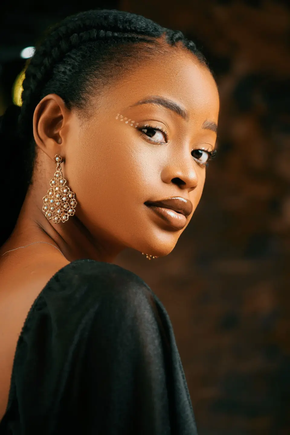 Woman with braided hair wearing a large gold filigree drop earring, portrait