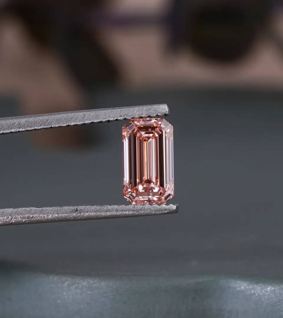 Pink emerald-cut diamond held in jeweler’s tweezers, close-up