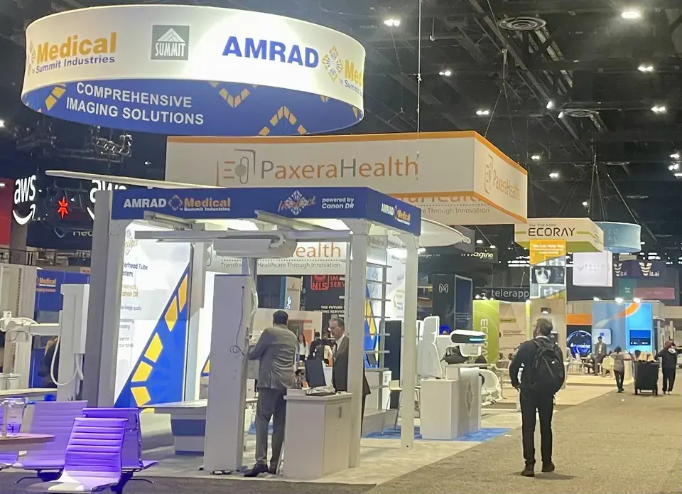 AMRAD Medical island booth by Purple Exhibits with X-ray equipment under a circular hanging sign