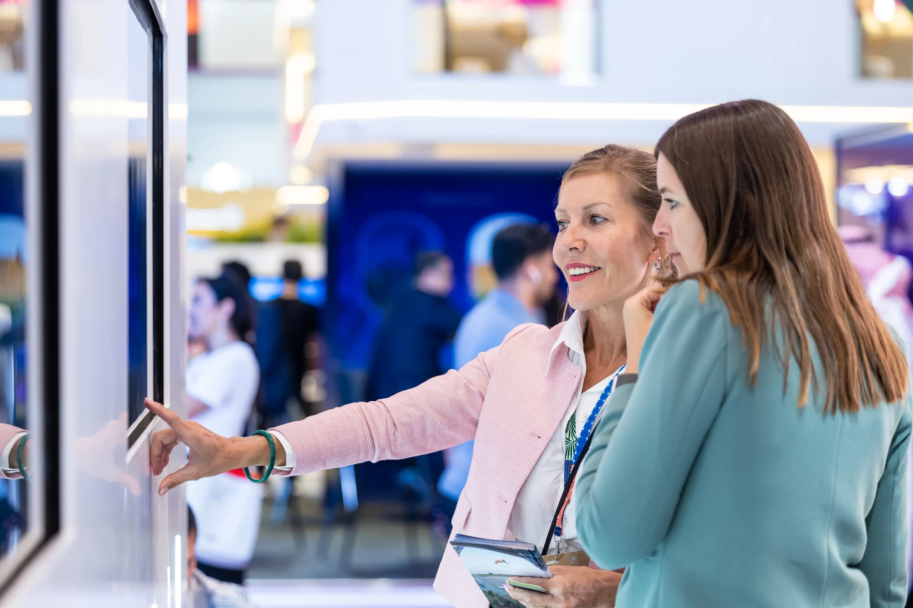 A touchscreen demonstration at Arabian Travel Market A woman in a pink blazer explains a touchscreen display to a visitor at Arabian Travel Market.
