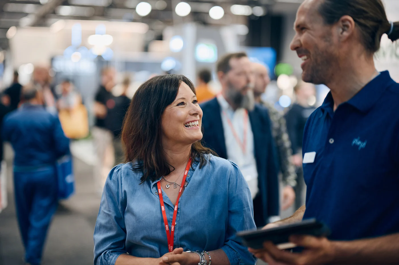 A smiling woman visitor talks with an exhibitor holding a tablet on the Elfack show floor.