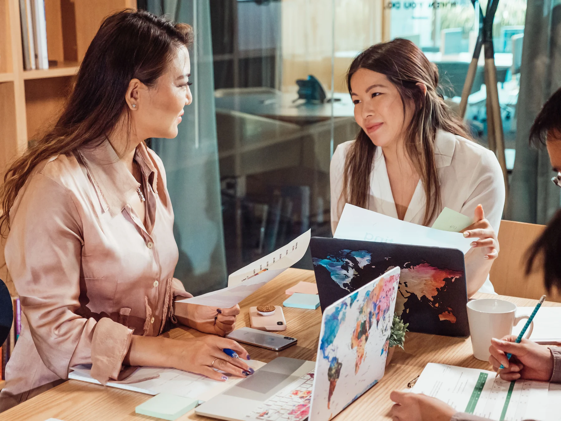 Women review printed information together beside open laptops during a team discussion.