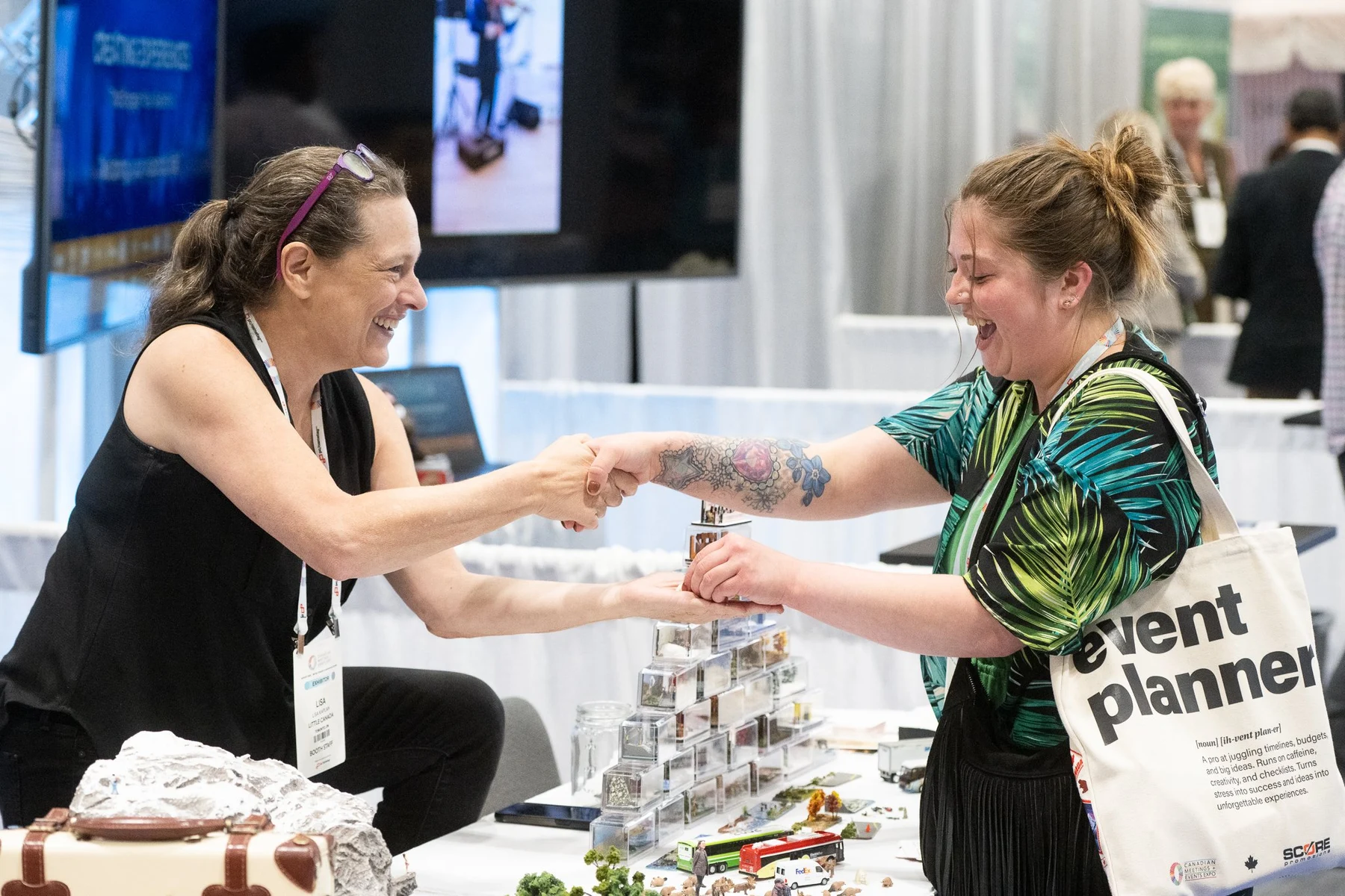 Two women smile and shake hands across an exhibit display at Canadian Meetings and Events Expo.