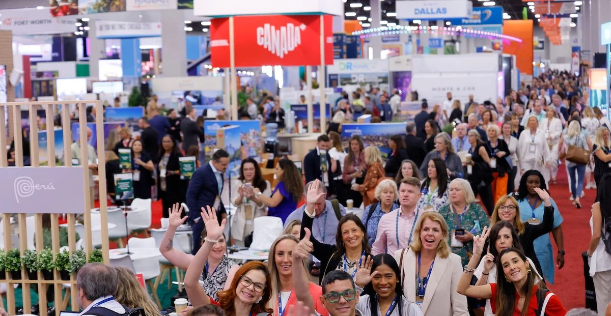 Visitor engagement in an IMEX America aisle Attendees wave and meet exhibitors along a crowded aisle at IMEX America, with Canada and Peru stands behind them.