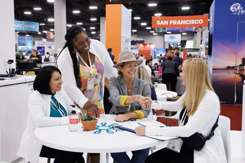 A small-group meeting at IMEX America Four women connect around a white meeting table on the IMEX America exhibition floor.