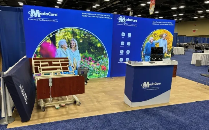 MedaCure exhibit with a hospital-bed demonstration, blue healthcare graphics, a reception counter and a monitor.
