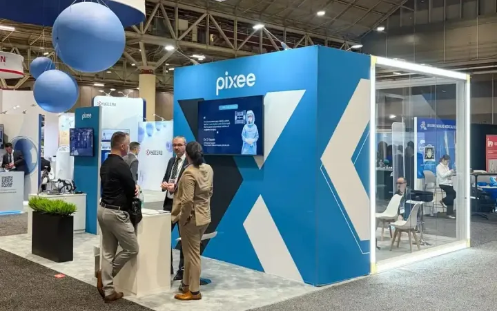 Visitors talking at Pixee Medical's blue exhibit beside a presentation screen and glass meeting room beneath a white hanging sign.