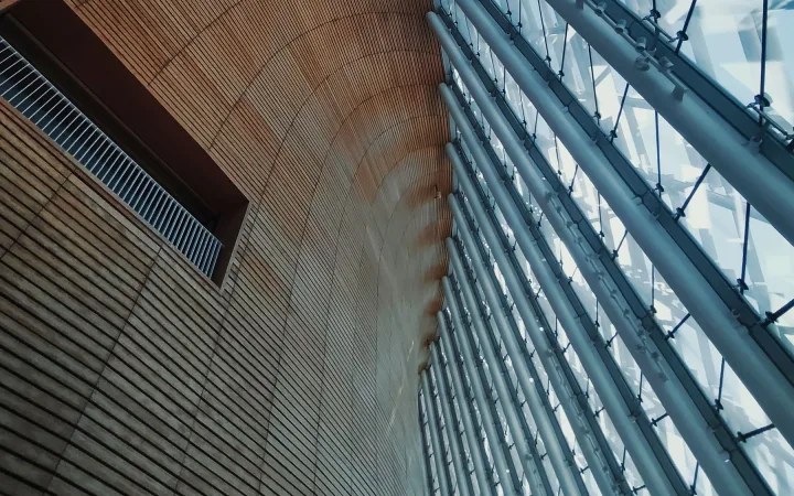 Sculptural timber walls meet a tall glass facade and exposed structural connections inside a modern exhibition center.