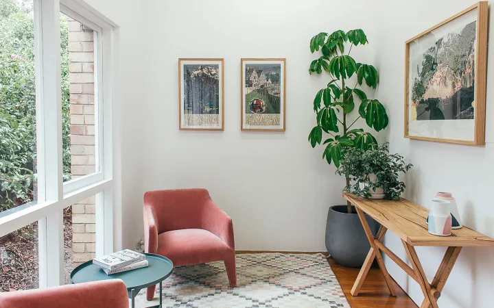Pink upholstered chairs, indoor plants and a wooden table beside large apartment windows.