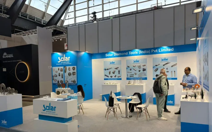 Solar Diamond Tools exhibit with blue-and-white walls, sample plinths, cutting-tool diagrams, meeting chairs and two visitors talking.