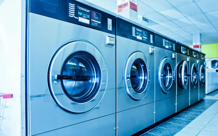 A row of stainless-steel washing machines inside a laundromat.