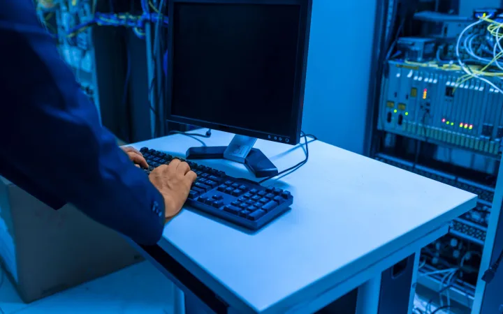 An IT professional works at a computer in a server room.