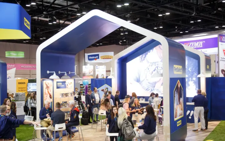 Visitors meet inside a blue-and-white PetSafe exhibit with product displays on the Global Pet Expo show floor.