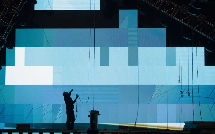 A stage technician works beside a large illuminated digital screen.