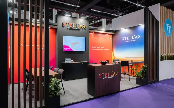 Stellar Entertainment exhibit with orange and blue wall graphics, a presentation screen, reception counter and meeting area framed by dark timber slats.