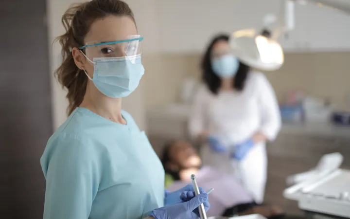 A woman dental professional wearing protective equipment holds instruments in a clinic.