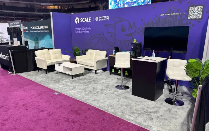 Spectral Compute exhibit with purple SCALE software graphics, white lounge seating, a large screen and a black reception counter.