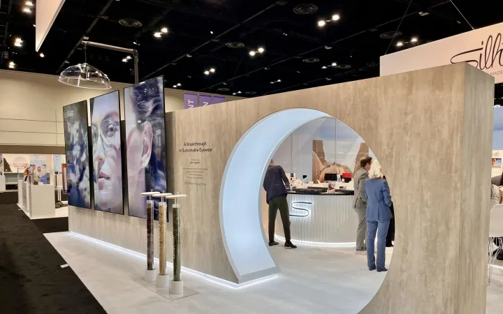 Silhouette eyewear exhibit with a pale wood facade, illuminated circular entrance and visitors at the counter.