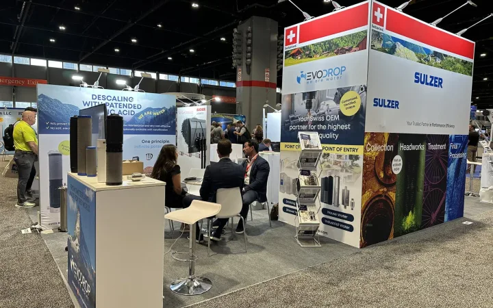 Swiss water-technology pavilion with Evodrop filtration products, Sulzer and Bucher Unipektin branding, sample counters and a seated visitor meeting.