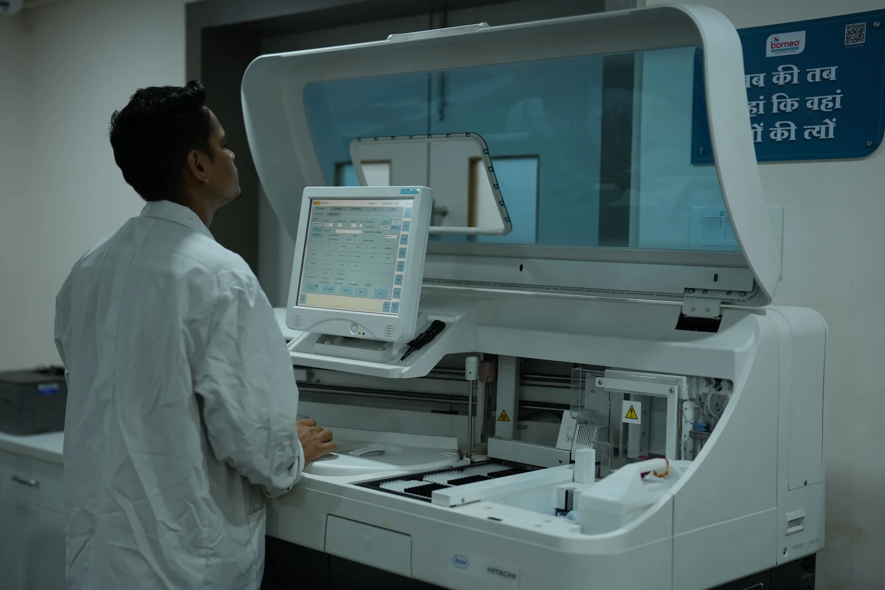 A laboratory technician operates a clinical analyzer.