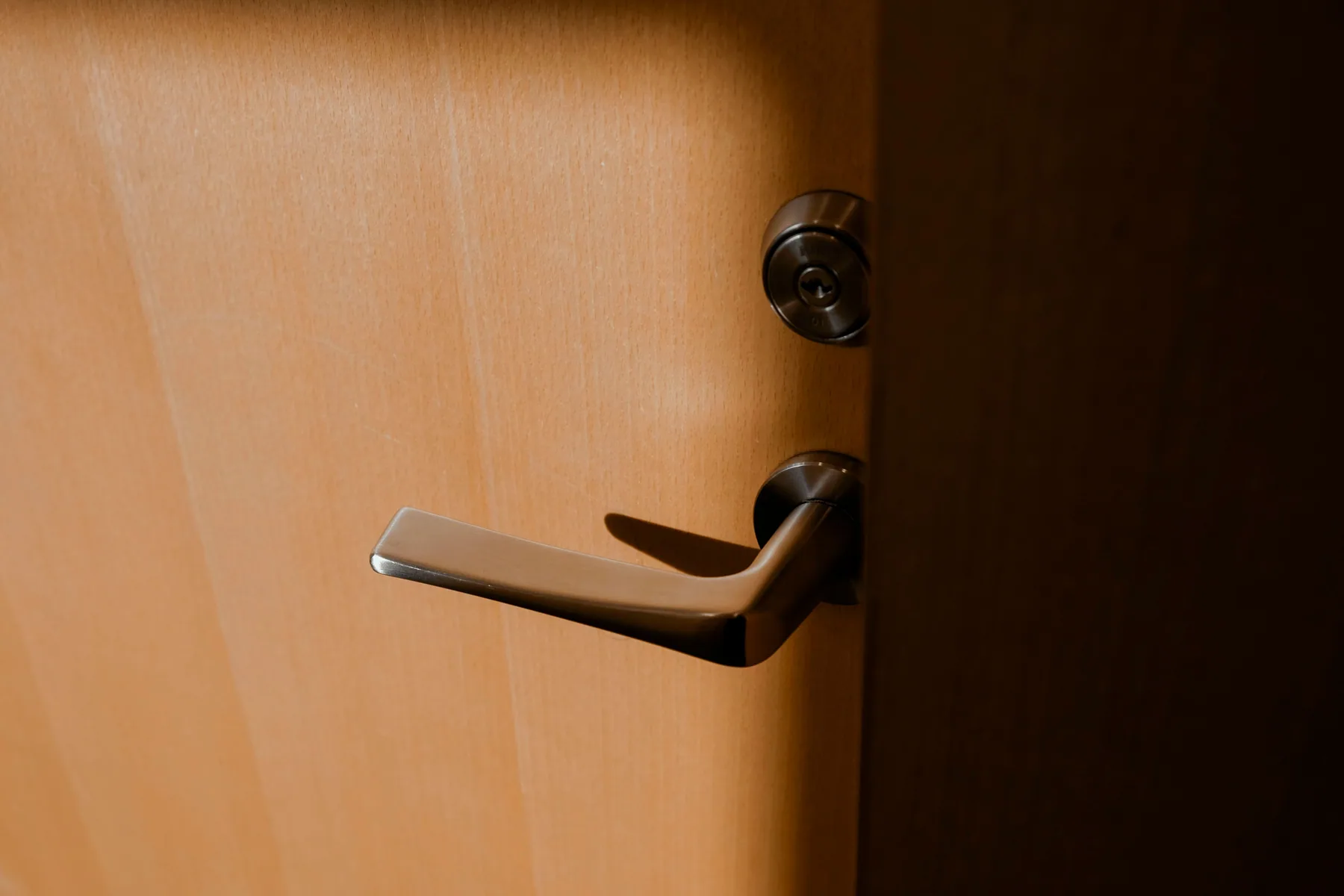 A silver handle and lock on a wooden door in warm light.