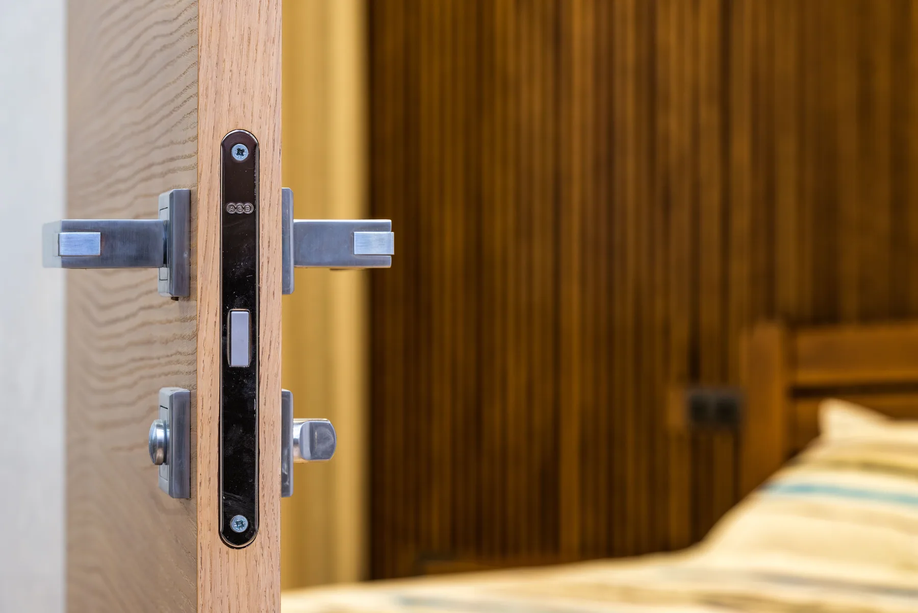 A modern wooden door with a metal handle and lock opens toward a bedroom.