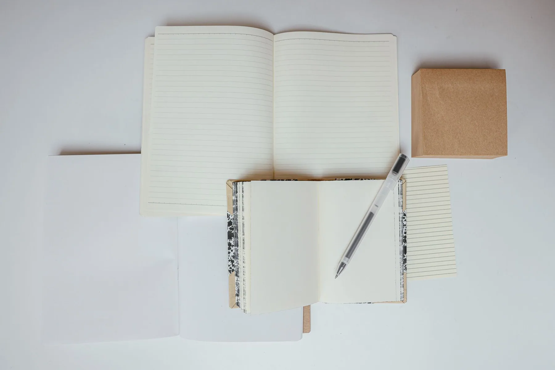 A pen lies across open notebooks on a white surface.
