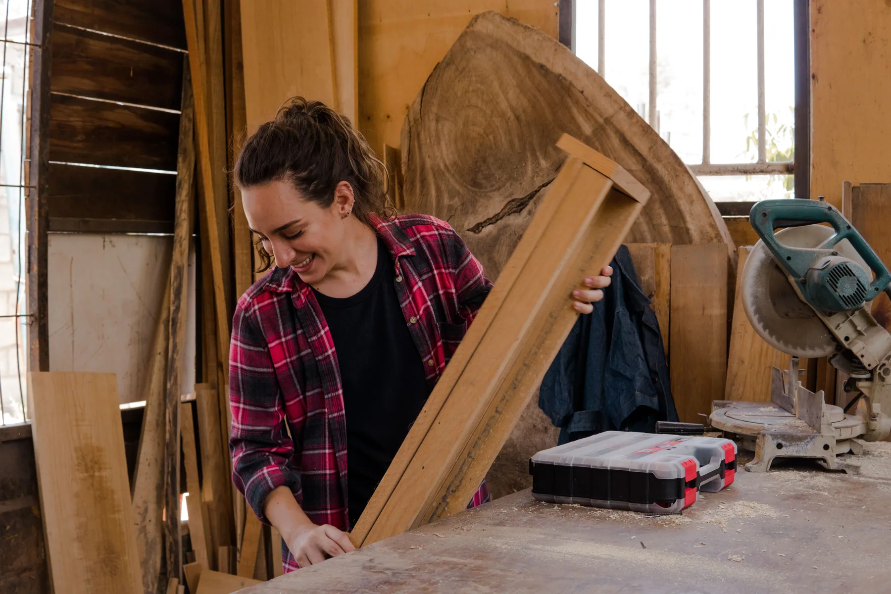 A woman handles a piece of wood in a workshop.