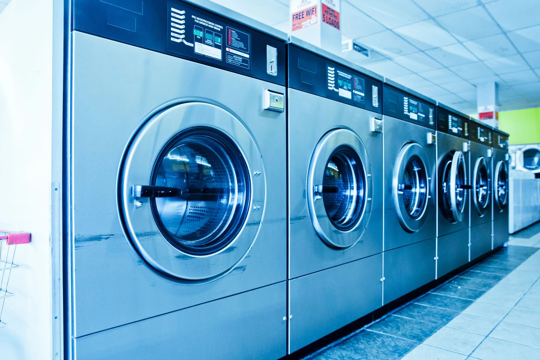 A row of stainless-steel washing machines inside a laundromat.