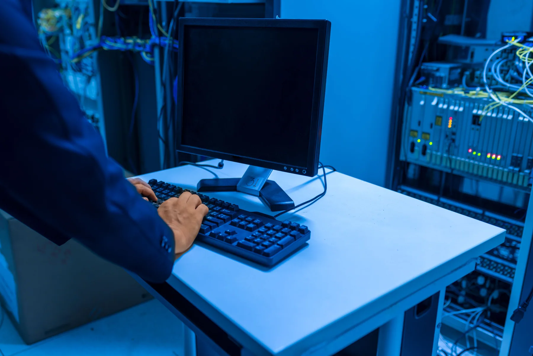 An IT professional works at a computer in a server room.