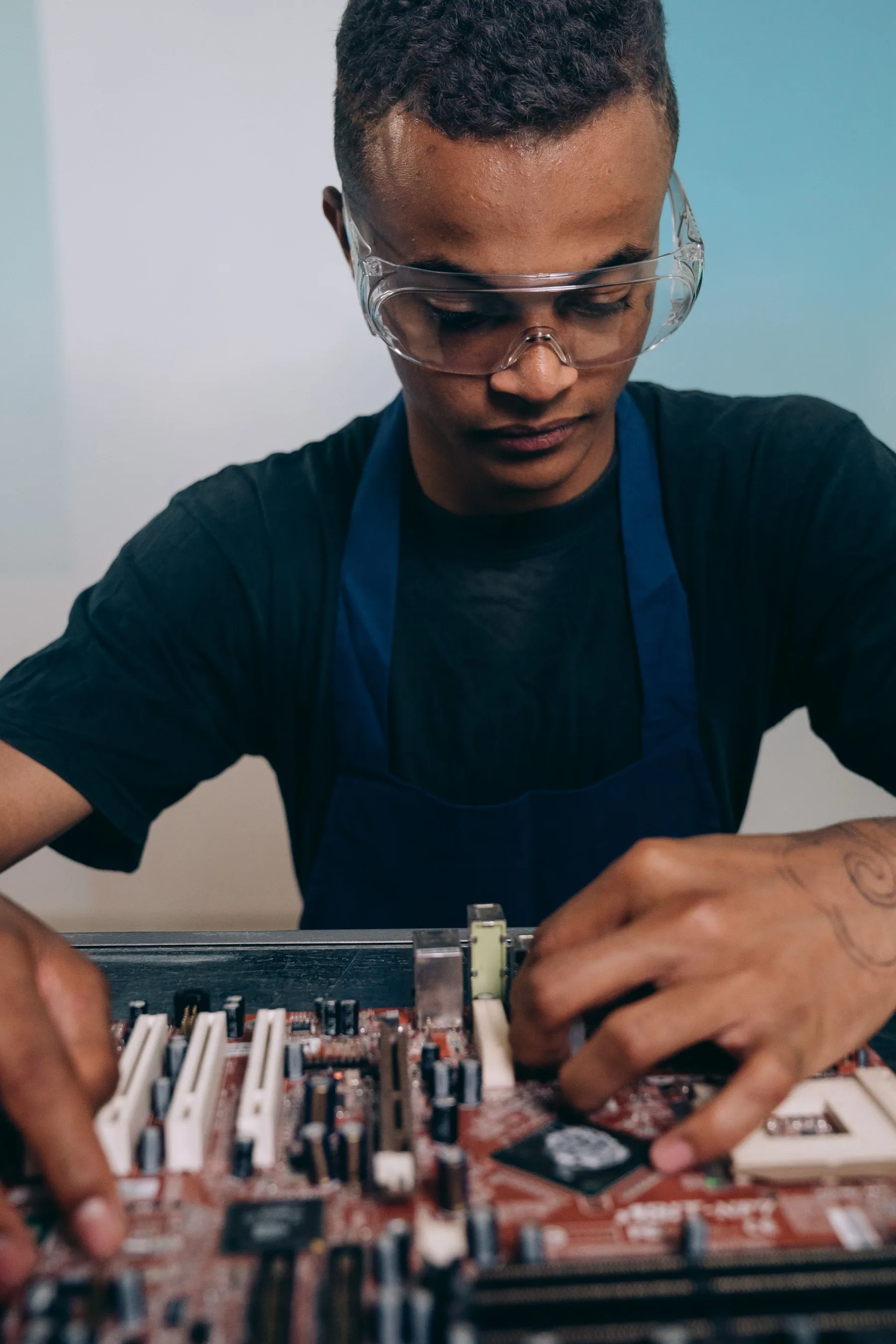 A technician works on a circuit board at an indoor workbench.
