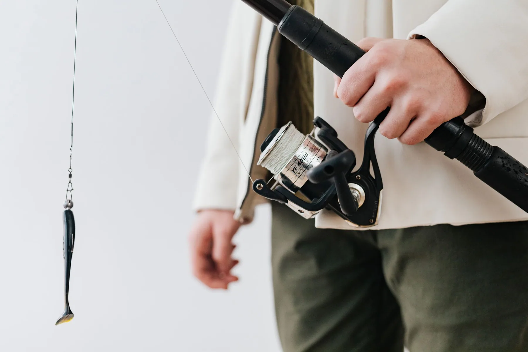 A hand holds a fishing rod with a lure and reel.