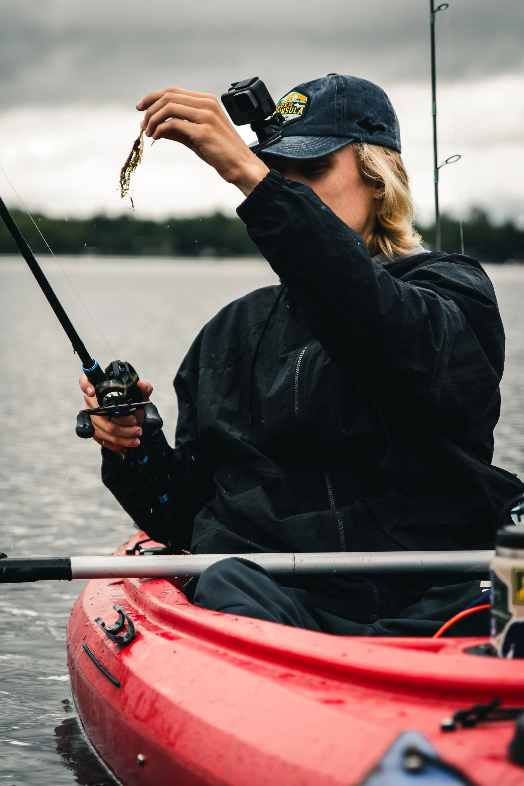 A woman fishes from a red canoe on a lake.