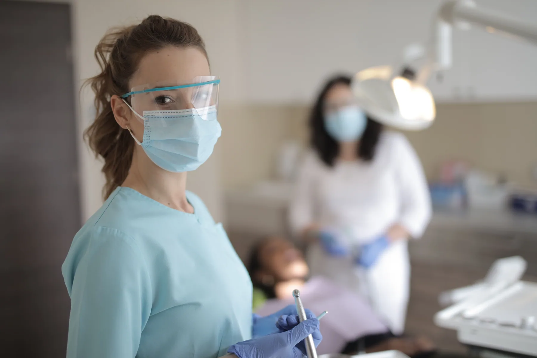 A woman dental professional wearing protective equipment holds instruments in a clinic.