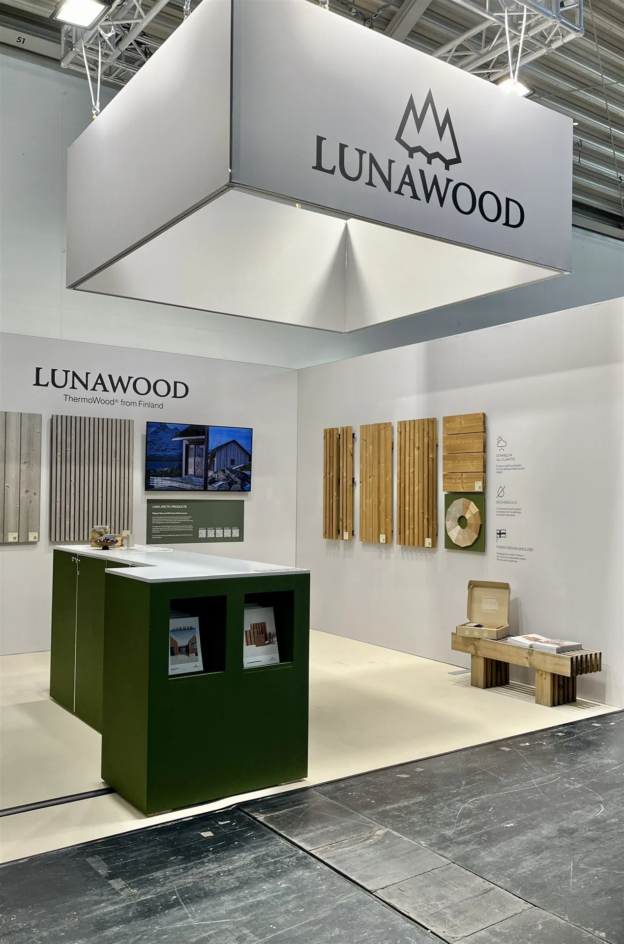 Lunawood exhibit with wood samples, a green counter and a suspended white brand sign.