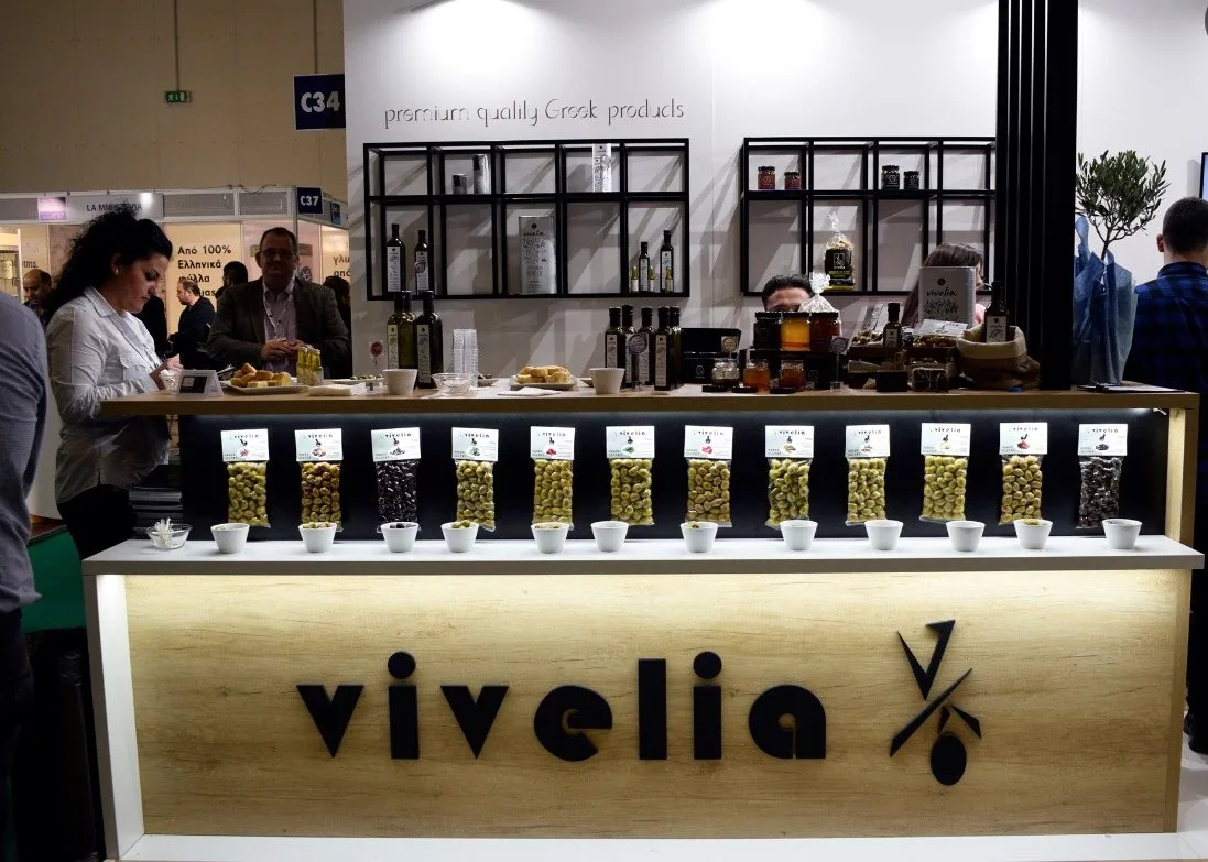 Vivelia Greek-food exhibit with olive products, tasting dishes and people behind the counter.