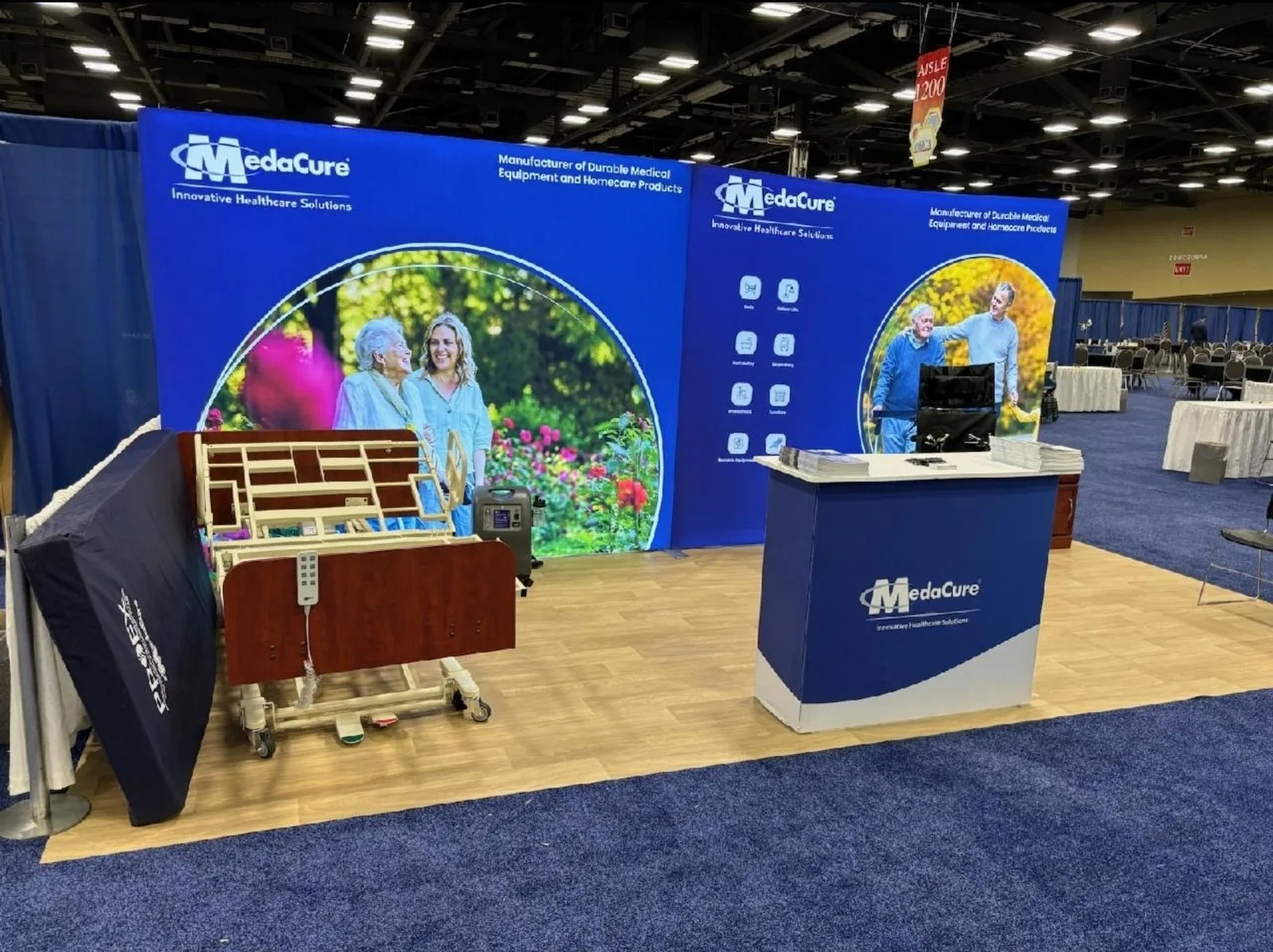 MedaCure medical-product booth with a blue backwall, care imagery, reception counter and a physical bed-frame display.
