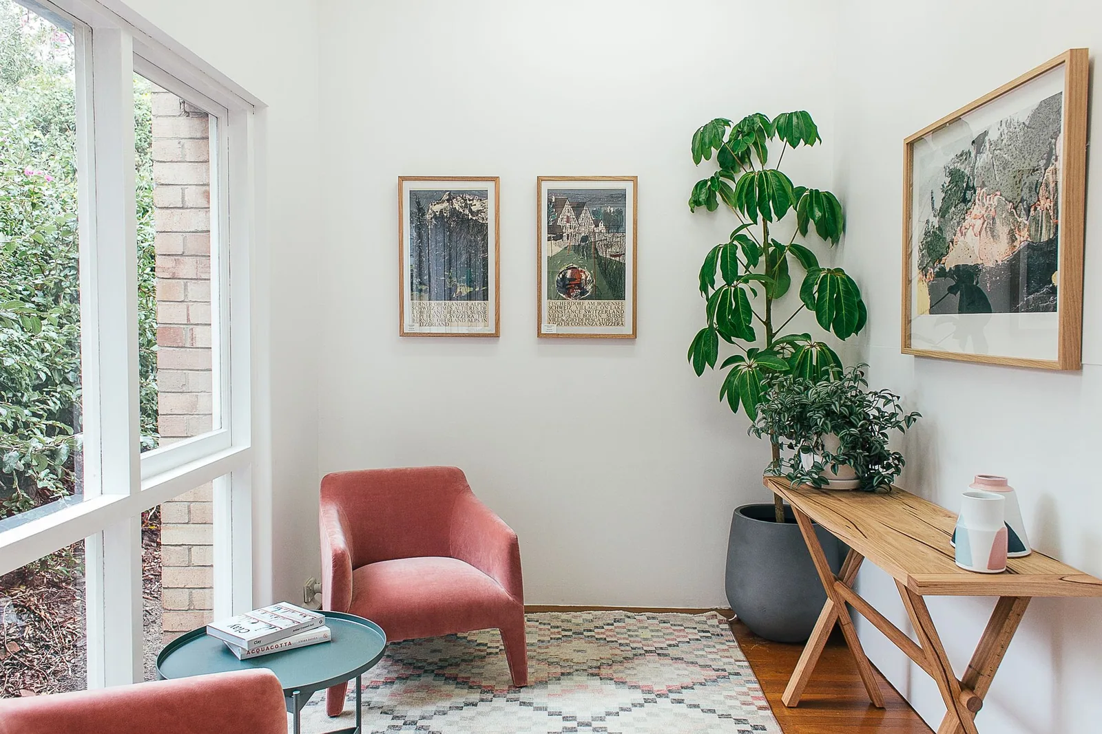 Pink upholstered chairs, indoor plants and a wooden table beside large apartment windows.