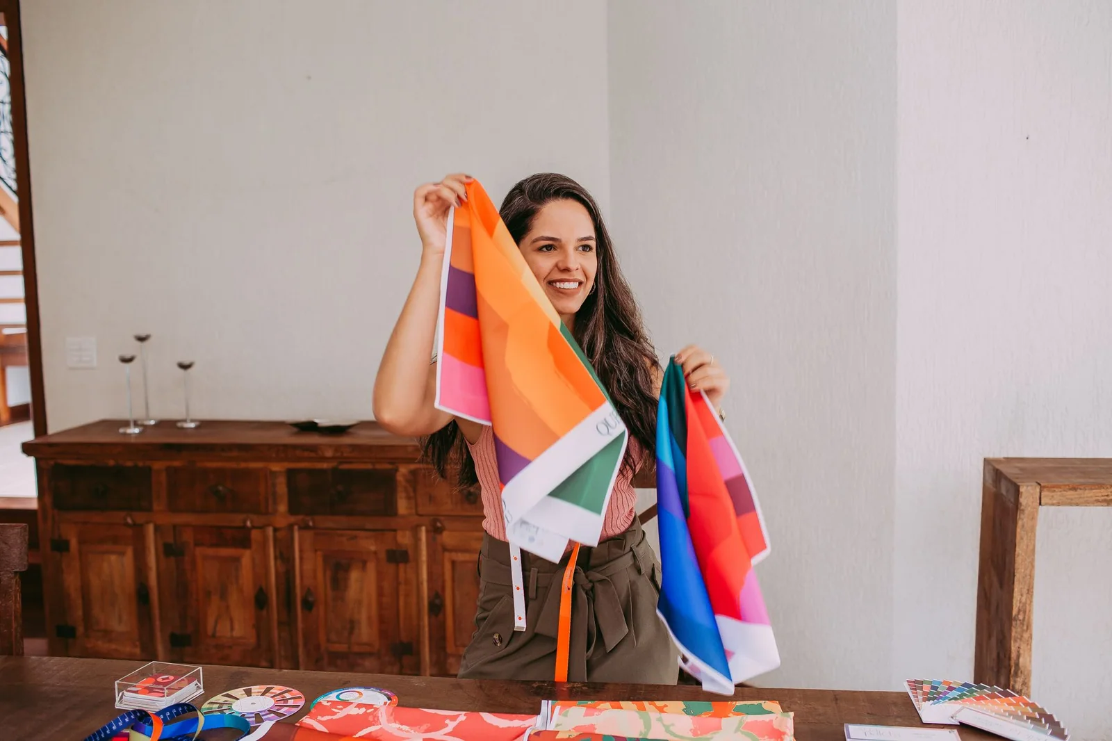 Smiling adult woman holding large colorful fabric pieces above a worktable with color cards.