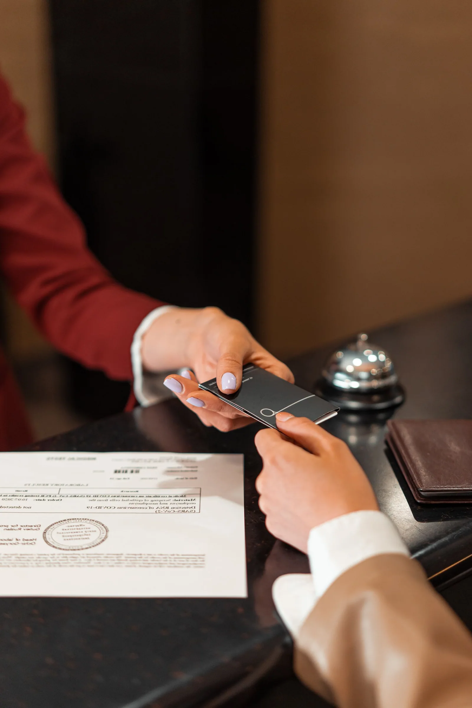Close-up of a hotel receptionist passing a key-card wallet to a guest at the reception counter.