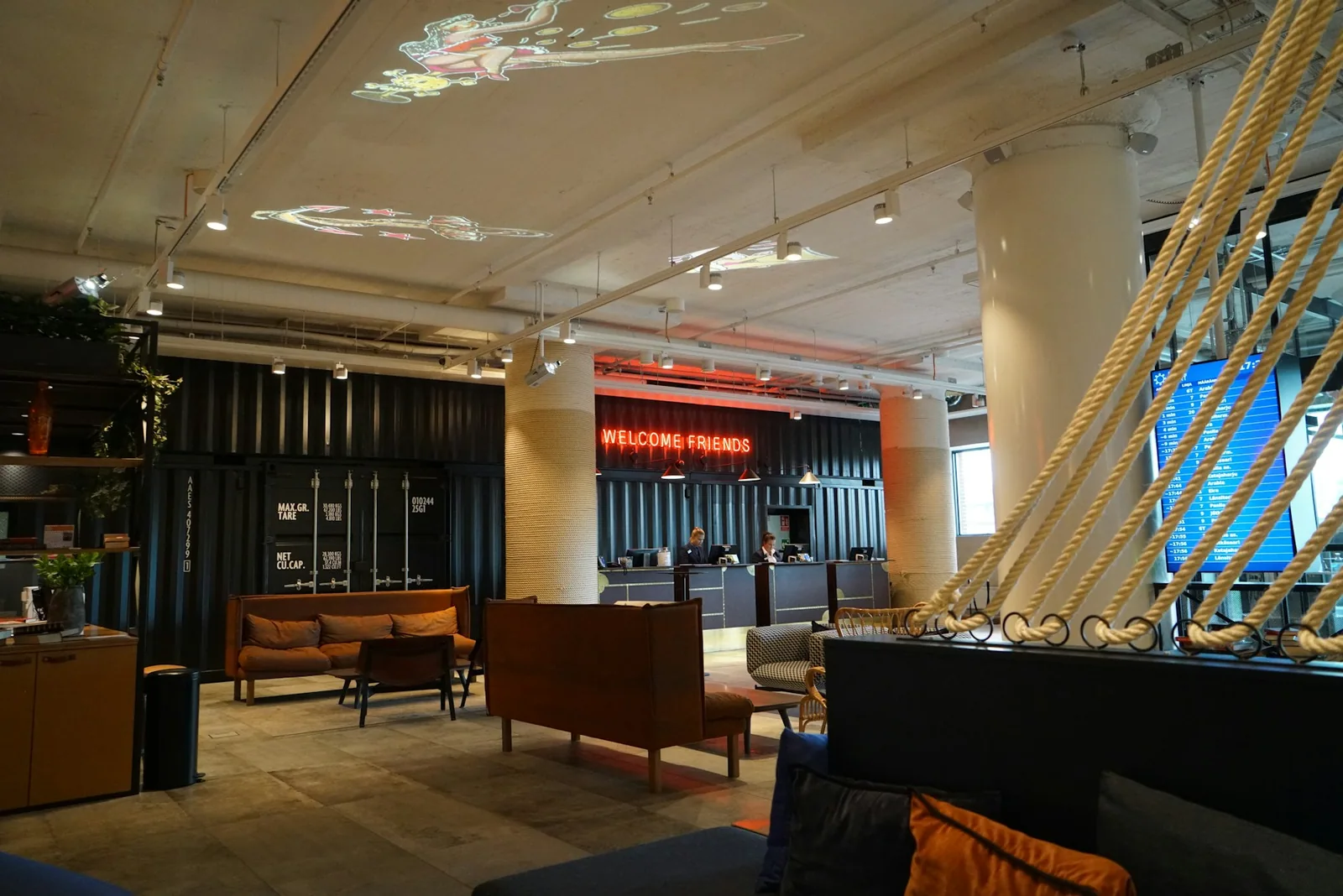 Hotel lobby with a reception desk, lounge seating, an information screen and projected ceiling graphics.
