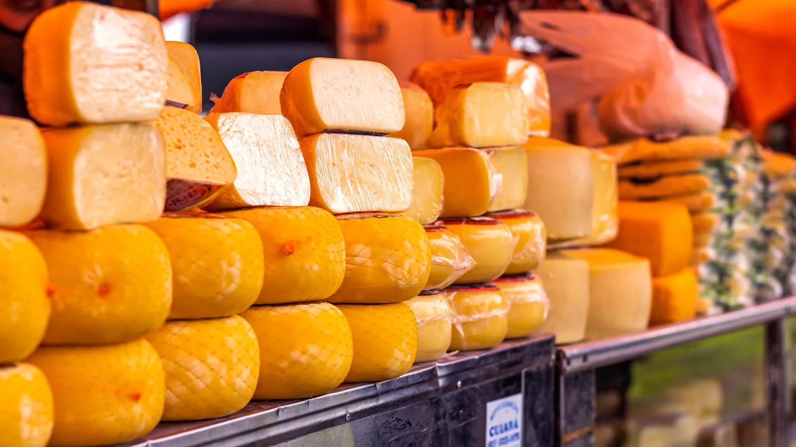 Assorted wrapped cheeses displayed together on a market shelf.