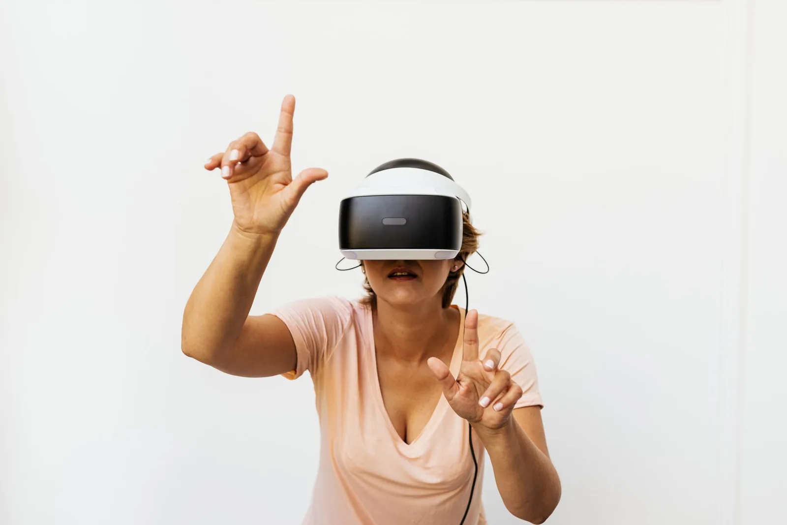 An adult woman in a peach shirt uses a virtual-reality headset and gestures with both hands.