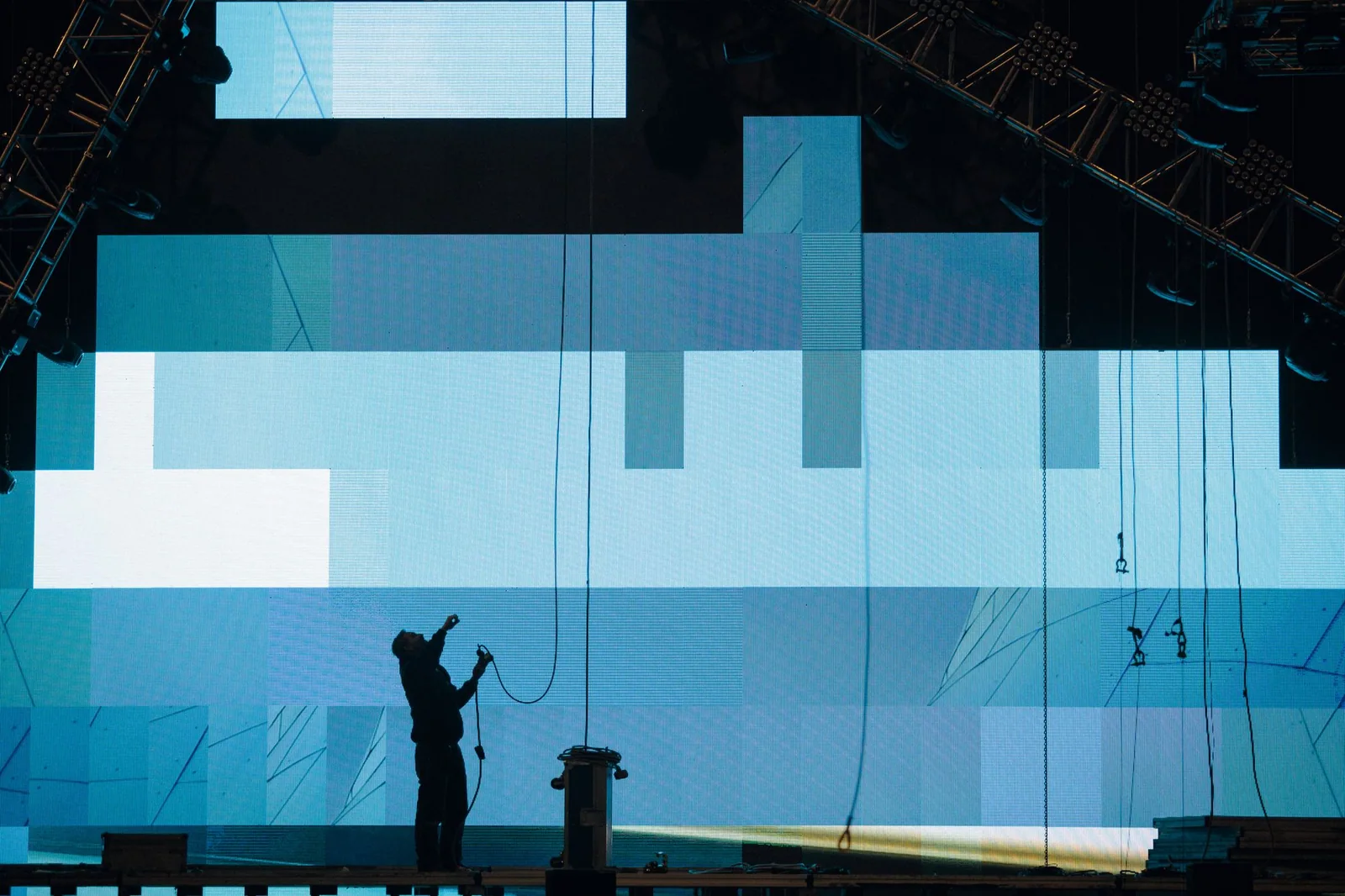 A stage technician works beside a large illuminated digital screen.