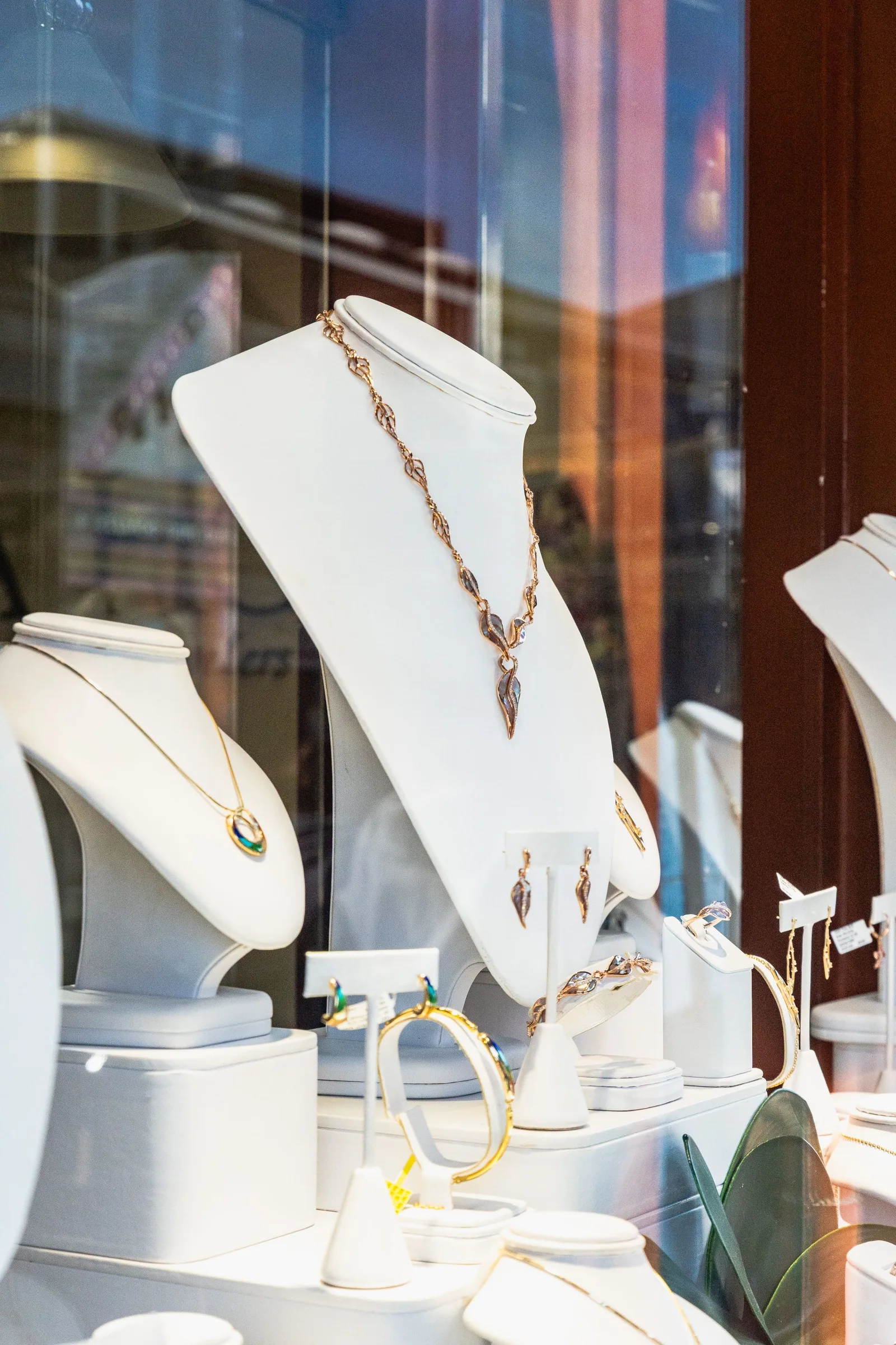 Jewelry displayed on necklace busts inside an illuminated boutique window.