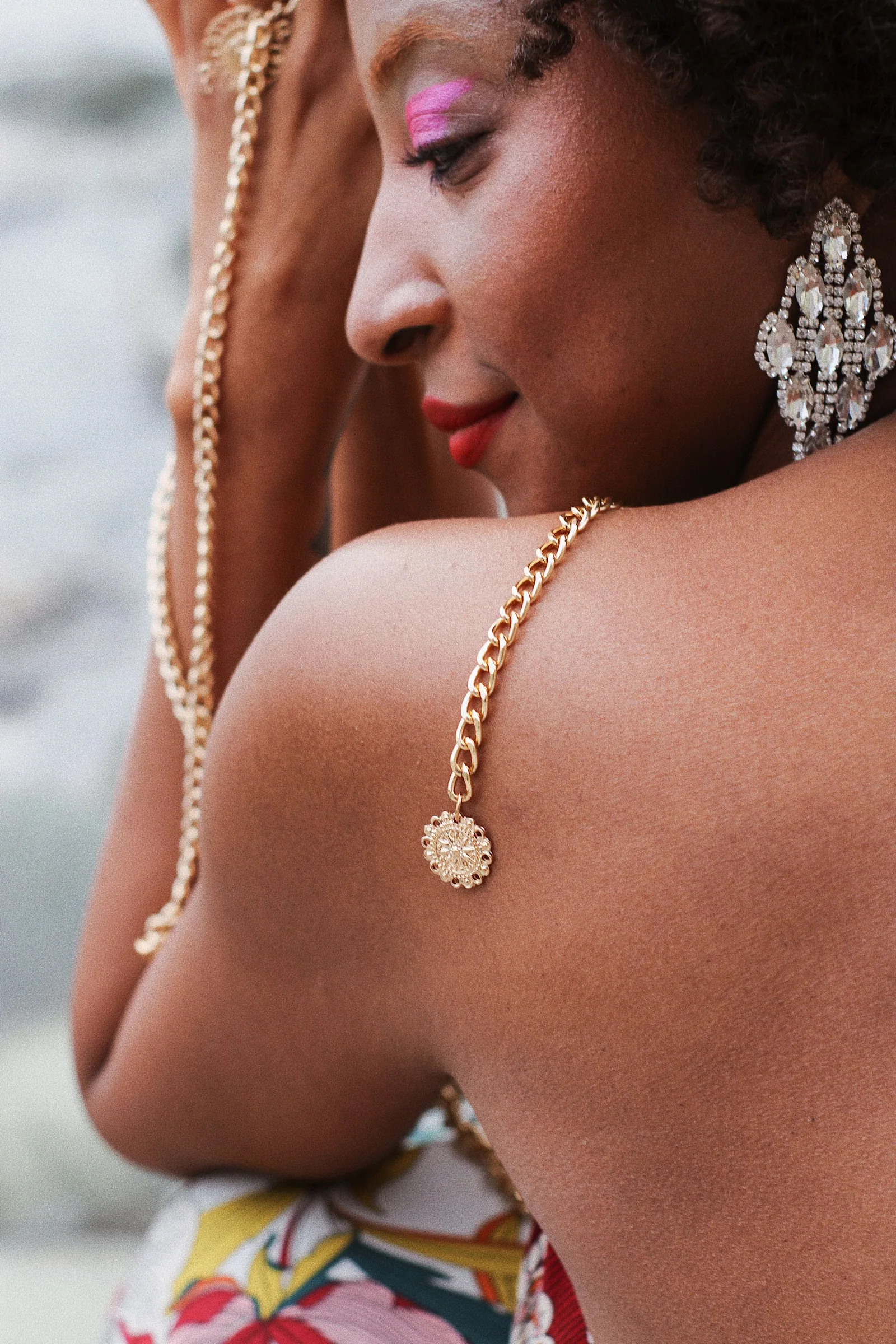 Close-up of an adult woman wearing sparkling drop earrings and holding a gold-toned chain across her shoulder.